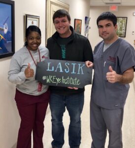 A Patient smiling for a photo after their LASIK procedure. They are holding a sign that reads "LASIK #WKEyeInstitute"